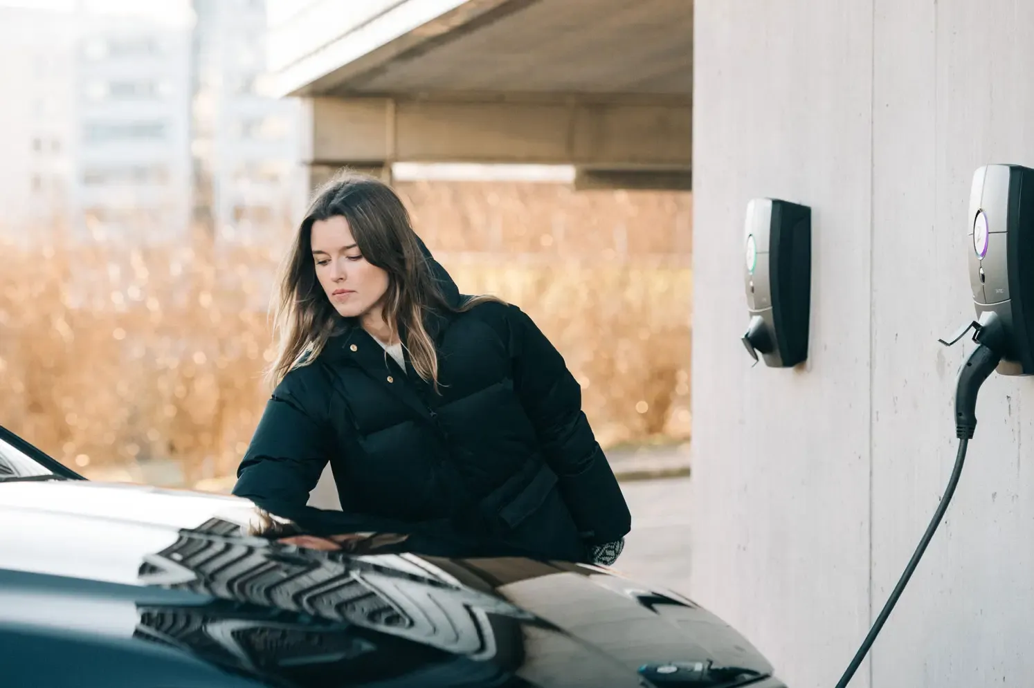 Boende med laptop vid sin bil framför en laddbox på ett flerbostadshus